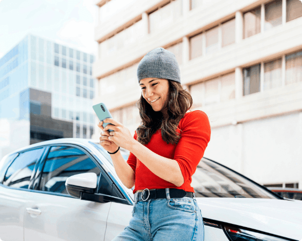 Person leaning against her vehicle while looking at her phone. 