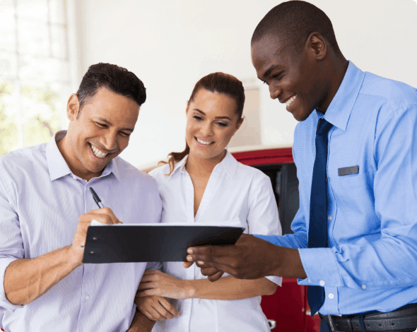 Couple signing a contract for a new car while a salesperson holds the clipboard. 