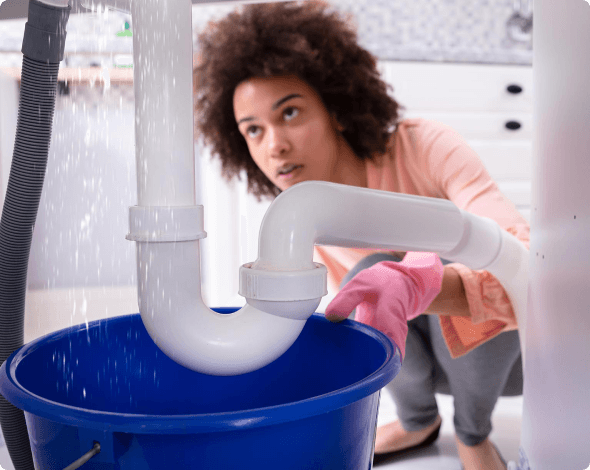 a woman looking under her sink at a leaky pipe