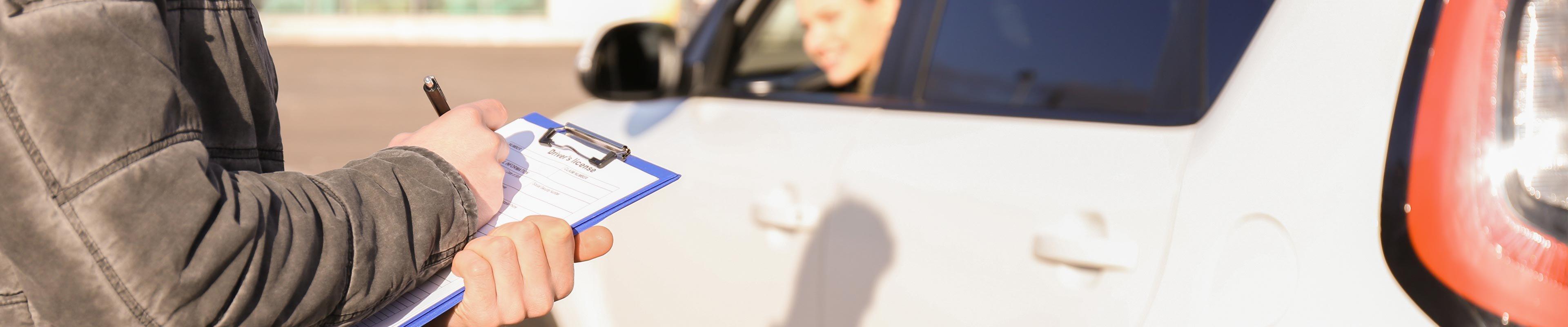 woman driving a car while a man is checking off her performance on a clipboard