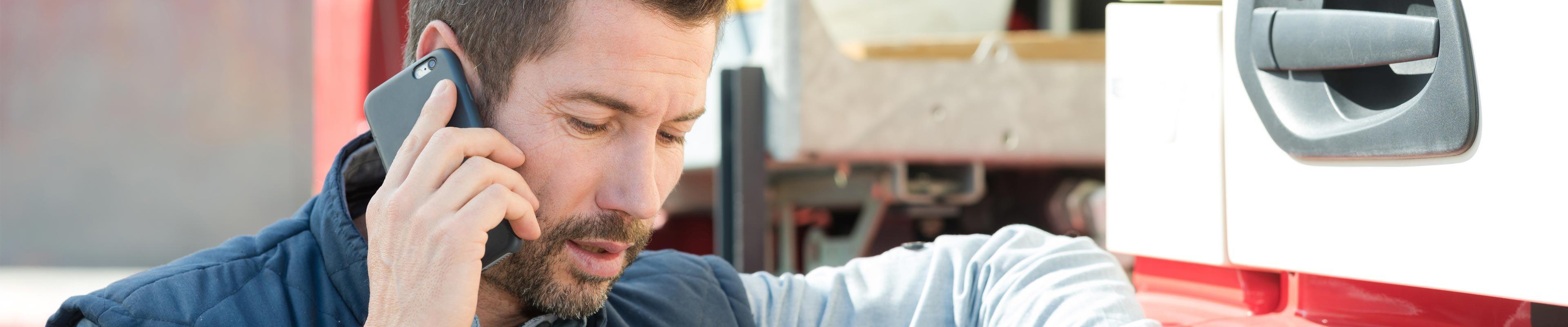 Man leaning up against a parked commercial truck using a cell phone