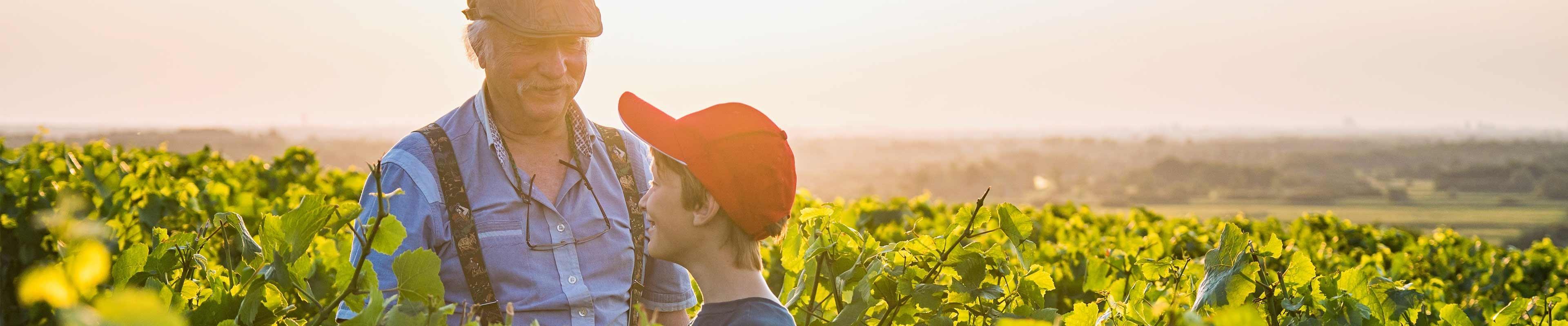 A white grandfather and his white grandson standing in a field of green on their family farm.