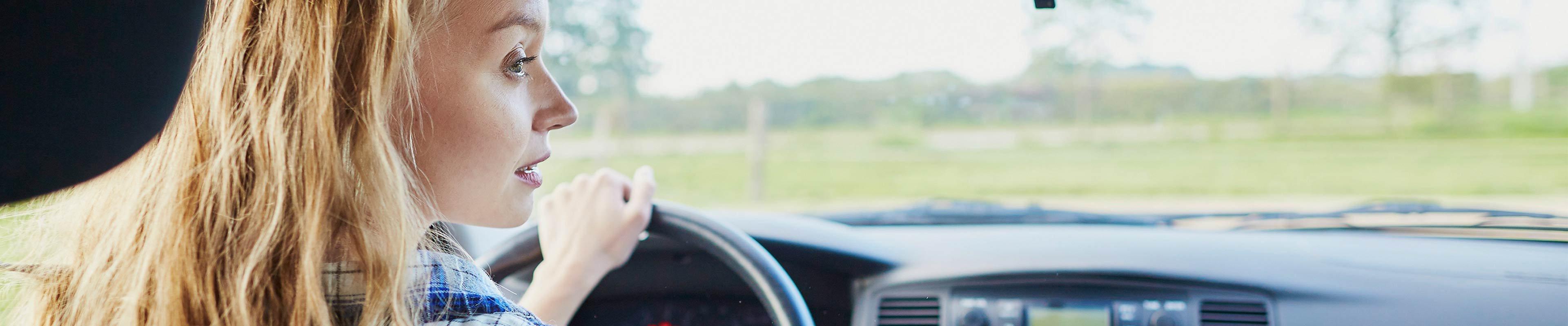 Young white blonde woman looking to her right while driving a car on a sunny day.