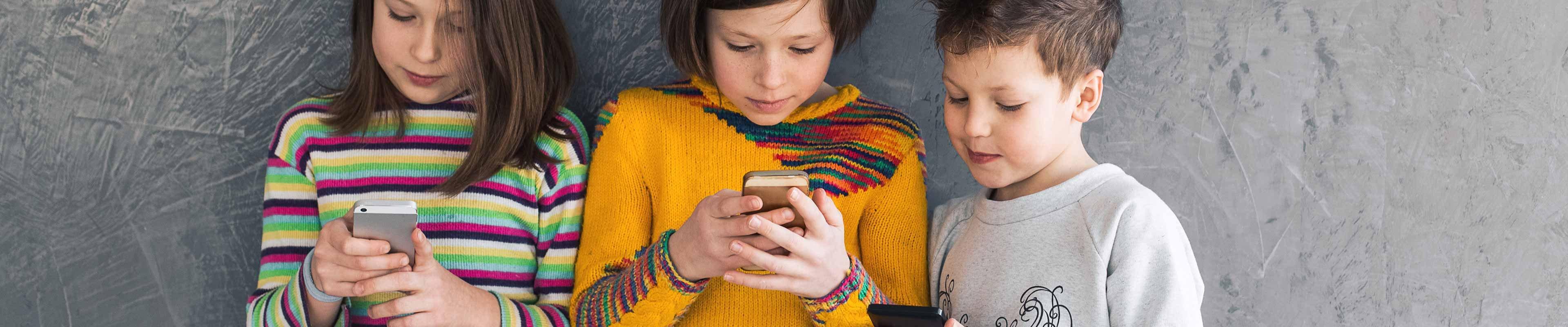 Three young kids looking at their cell phones.