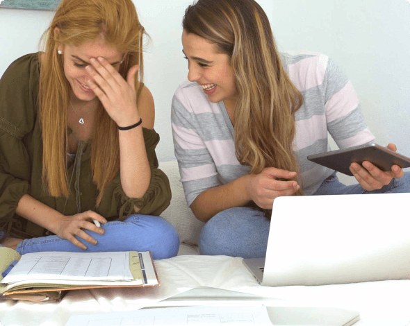 Image of two college roommates laughing with their laptops and tablets.