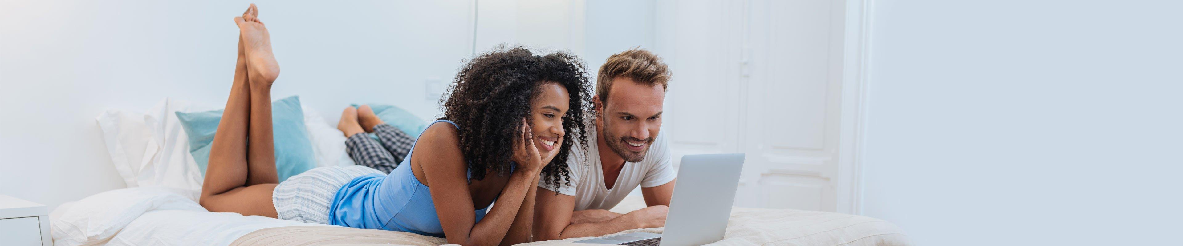 Young couple laying on bed and researching insurance on computer.