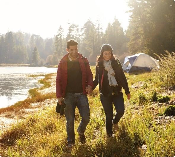 a man and woman standing in a grassy area next to a body of water